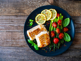 Wall Mural - Fish dish - fried cod fillet with asparagus on wooden table 