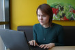 © Stanislav - Beautiful young girl sitting in a cafe at a table with a laptop. Works at the computer and types on the keyboard. Looks at the screen with an emotional expression. On the face is an expression of