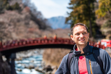 Wall Mural - Nikko, Japan mountains and famous red bridge landmark in blurry background in Tochigi prefecture in Japan with young happy tourist man smiling