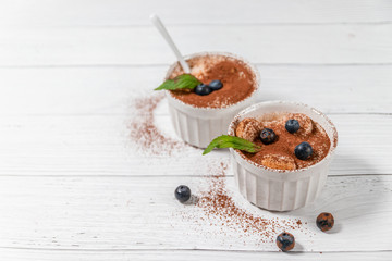 Wall Mural - Classic tiramisu dessert with blueberries, mint in white jar on grey background. Copy space.