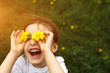A little girl of European appearance with light hair puts yellow dandelion flowers to her eyes and enjoys the summer, sun and warmth, laughing with her mouth open. Hello summer, place for text