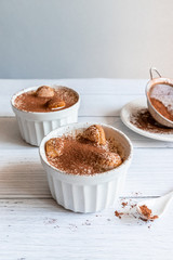 Wall Mural - Delicious tiramisu dessert with cocoa and savoyardi cookies in white ceramic jars on a gray background. Vertical photo