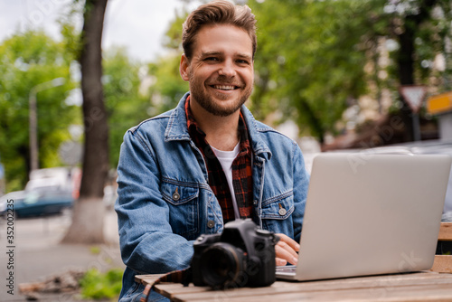 Fotomural Happy freelancer professional retoucher photo editor improves photos on a laptop, smiles and enjoys doing what he loves