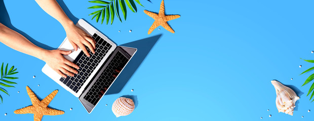 Person using a laptop computer with summer theme objects - flat lay