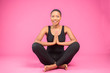 © Confidence - beautiful african female model, sitting in a meditation pose, hands together, legs crossed, smiling, on a plain background