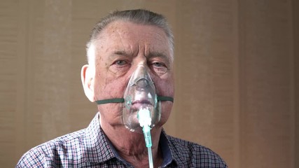 the man wearing breathing mask is sitting and deeply breathing in and out. portrait of the old man w