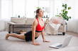 © Admiral - Online yoga workout at home. Attractive young woman doing stretching in living room. Sport, entertainment and education on the Internet.