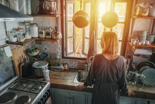 Mature Woman Standing Next To A Window In An Old Narrow Cluttered Kitchen
