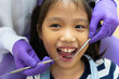 dentist using dental tools to clean teeth of asian child and treat tooth decay in the clinic with asisstance standing behind the patient. dentistry and healthcare concept