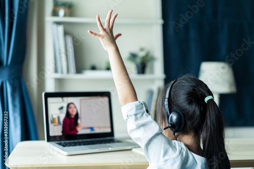 Fotomural Homeschool Asian little young girl student learning virtual internet online class from school teacher by remote meeting due to covid pandemic