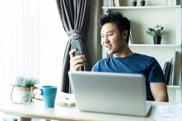 Asian young man play online game on mobile smartphone in living room.