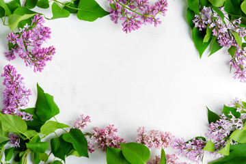 Wall Mural - Greeting frame from fresh lilac flowers with green leaves on a light grey marble background. Top view.