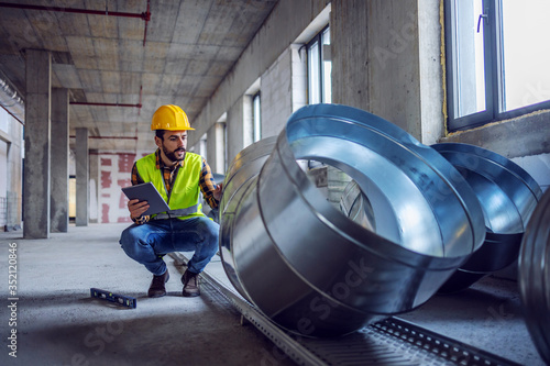 Fotomural Highly motivated caucasian construction worker in work wear crouching next to exhaust pipes and checking on their quality