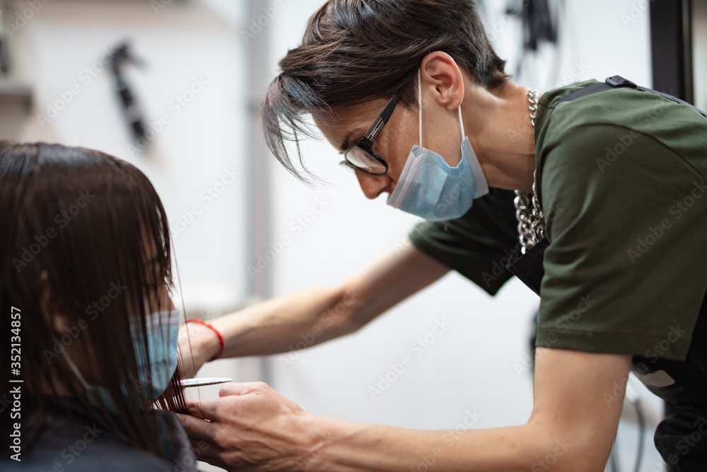 Hairdresser and girl child customer in a salon with medical masks during virus pandemic. Working with safety mask. - obrazy, fototapety, plakaty 