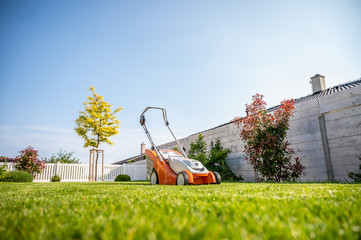 Wall Mural - A lawn mower on a lush green lawn surrounded by flowers. The back yard of the house.