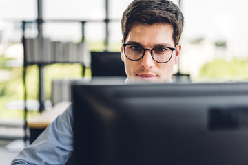 Handsome confident businessman relaxing looking at technology of desktop computer monitor while sitting on chair.Young creative coworkers business people working and typing on keyboard at office