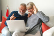 © Art_Photo - Senior couple family having good time using laptop computer together.Happy elderly husband and wife checking social media and reading news or shopping online while sitting on sofa at home.Retirement