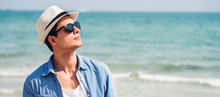 Portrait Of Smiling Happy Handsome Man Model Enjoying And Relax In Fashionable Sunglasses And Hipster Summer Straw Hat Standing On The Tropical Beach And Looking At Camara.Summer Vacations And Travel