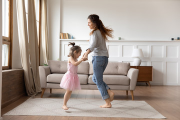 happy mother and little daughter wearing princess dress holding hands, dancing in modern living room