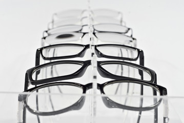 Many glasses on a white background. Glasses are stacked in a row on a transparent shop window. Glass stand on gray table. Sale and exhibition of optics.