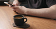 © GCapture - unrecognizable man sitting at the walnut table with smartphone and drink fresh espresso