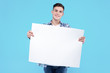 © Monstar Studio - Young man in white t-shirt, checkered shirt is holding blank empty paper canvas. Guy student is smiling, standing on blue background. Template for advertising, greeting, invitation. Emotional portrait