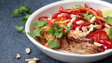 Wall Mural - Eating pad thai noodles with chicken, peanuts and vegetables in bowl, dark background.