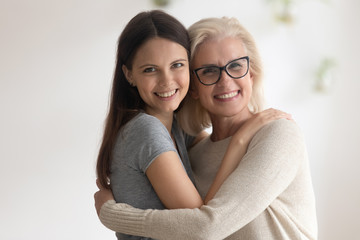 Wall Mural - Portrait of smiling senior mother and adult daughter embrace show gratitude and love, happy caring mature mom and grownup millennial girl child hug look at camera posing, good relations concept