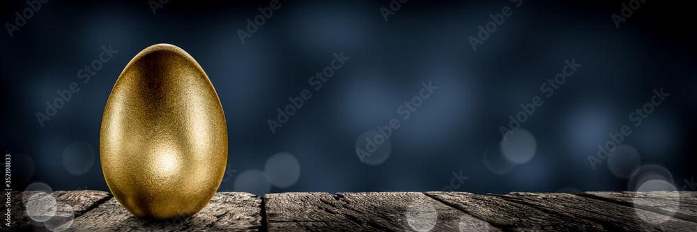 Golden Nest-Egg On Wooden Table With Blue Background - Investment / Retirement Plan Concept - obrazy, fototapety, plakaty 