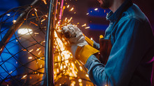 Close Up Of A Talented Innovative Artist Using An Angle Grinder To Make An Abstract, Brutal And Expressive Metal Sculpture In A Workshop. Contemporary Fabricator Creating Modern Steel Art.