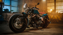 Custom Bobber Motorbike Standing In An Authentic Creative Workshop. Vintage Style Motorcycle Under Warm Lamp Light In A Garage.