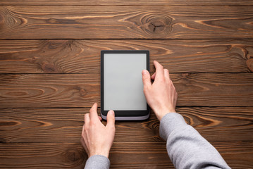 A modern black electronic book with a white blank screen with male hand on a dark wooden background top view