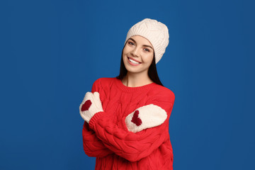 Poster - Young woman wearing warm sweater, mittens and hat on blue background. Winter season