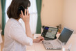 在宅勤務中の女性のイメージ、ノートPC、タブレットを使いながら携帯電話で仕事の話をする女性