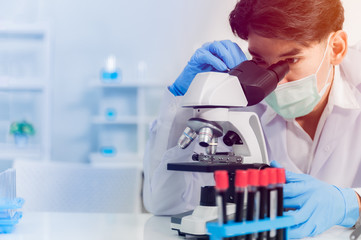 Asian man scientist wear medical face mask and working by using microscope.