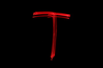 Wall Mural - Long exposure photograph of the letter t in neon red colour fairy lights against a black background. Light painting photography. Part of an alphabet series. 