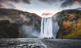 Impressively beautiful nature of Iceland during sunset. Skogafoss waterfall is one famous natural landmark and travel destination place of Iceland.  Tourists ride horses near famouse waterfall.