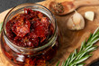Sun-dried tomatoes with garlic, rosemary and spices in a glass jar on an olive wood cutting board