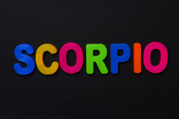 Scorpio text. Zodiac sign written in bright multi-colored cheerful letters on a black dramatic background. Low dark key