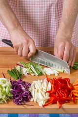 Close up of hands chopping scallions on a wooden board. Healthy food preparation concept