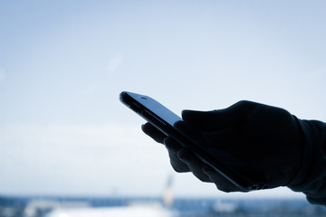 Hand silhouette holding cellphone over empty light background. Anonymous person with smart phone, password protection, identity theft concepts. Cold blue tones applied