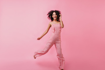 Wall Mural - Bright, brave girl in great mood jumping in studio. Photo taken on pink background of cute model in stylish summer outfit