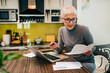 © bnenin - Senior woman doing paperwork at home.