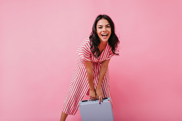 Wall Mural - Laughing girl with dimples on cheeks emotionally posing for full-length portrait with blue luggage