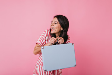 Wall Mural - Cheerful young woman is having fun and genuinely laughing on isolated background. Girl makes prank taking someone else's blue suitcase