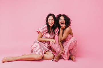 two girls with dark hair, one with straight and other with curly, dressed in soft and lovely pajamas