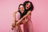 Fototapeta  - African sisters with dark curls are having fun in wonderful mood. Portrait of embracing girls with beautiful appearance