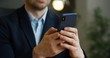 © VAKSMANV - Close up of smartphone in hands. Businessman tapping and scrolling on mobile phone in office.