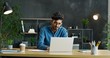 Young Arab busy male office worker sitting at table, working on laptop computer and considering.