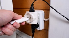 Overloaded Outlet With An Extension And Many Sockets Plugged In, A Hand Plugging A Socket Into The Outlet, Risk Of Fire And Short Circuit In A Wooden House